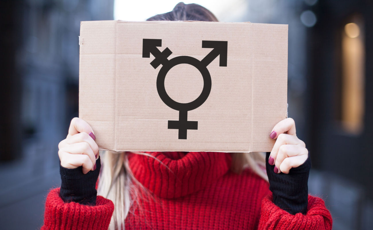 A person holds up a sign with the transgender sign on it