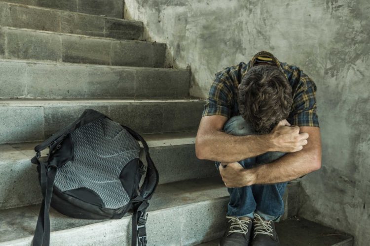 A teen hugging his knees on some steps