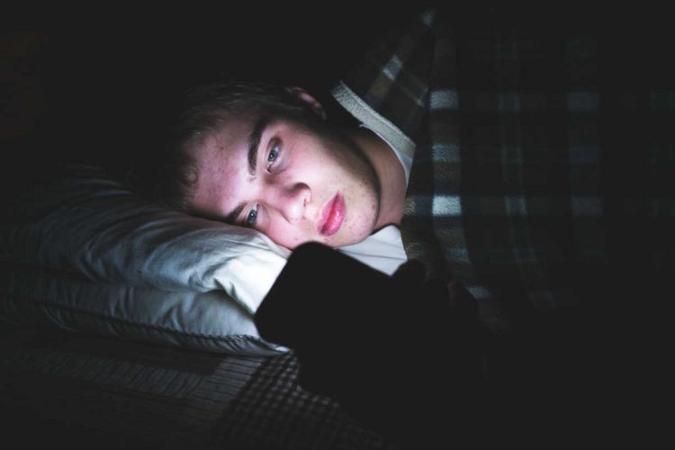 A teenager looking at his phone in bed
