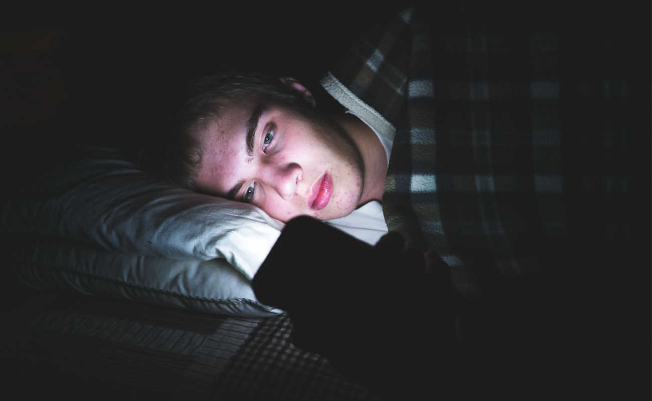 A teenager looking at his phone in bed