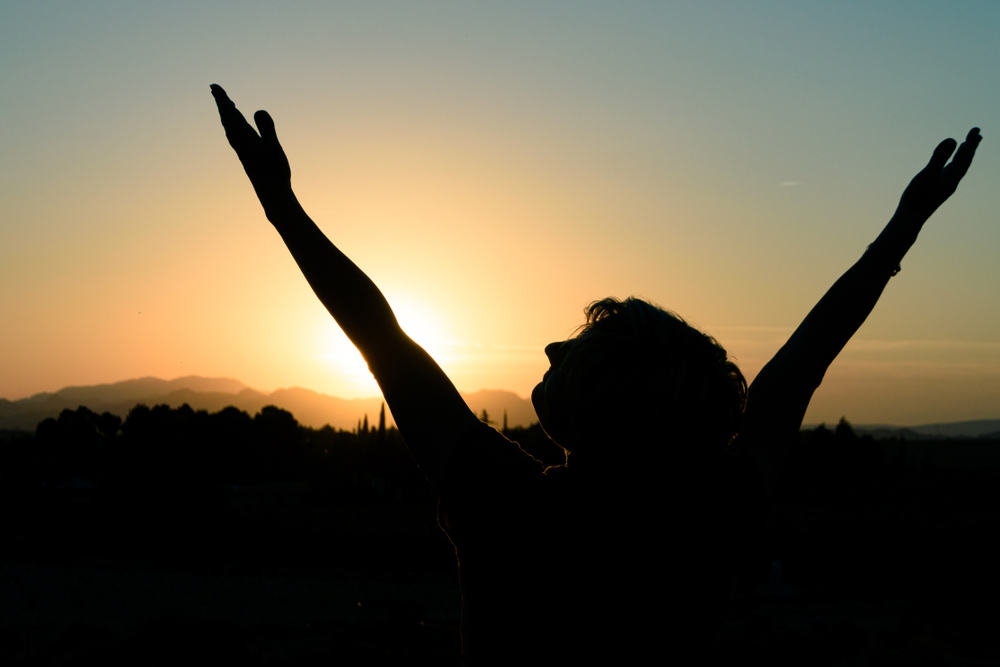 A woman holds her hands up in the sunset
