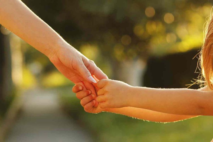 A parent holding their child's hand in the sunset light