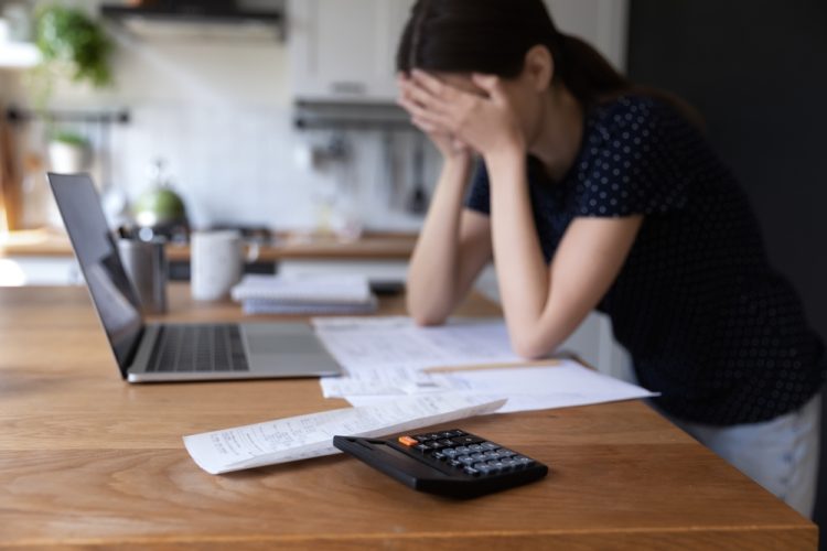 A woman holding her head in her hands with a computer in front of her and a calculator