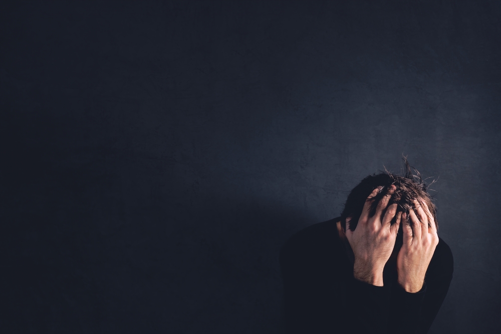 A man holding his head in his hands against a dark wall