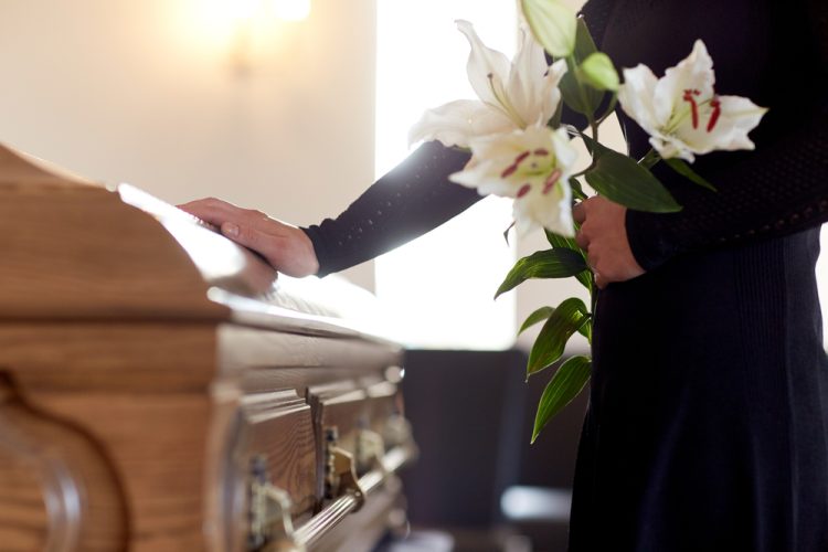 A person holding lilies and touching a coffin